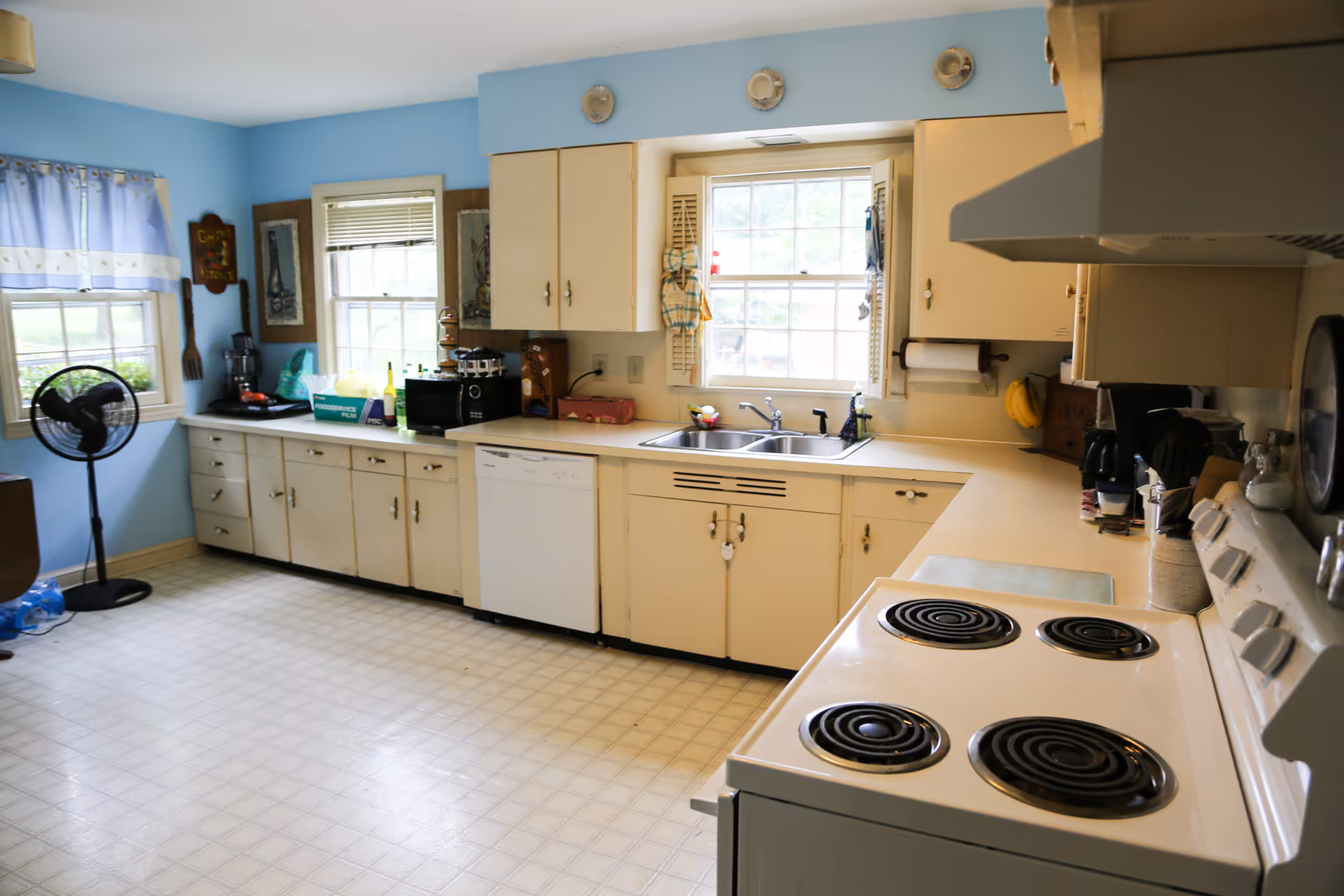 Bright, airy kitchen with white cabinets, a sink, stove, and large windows.