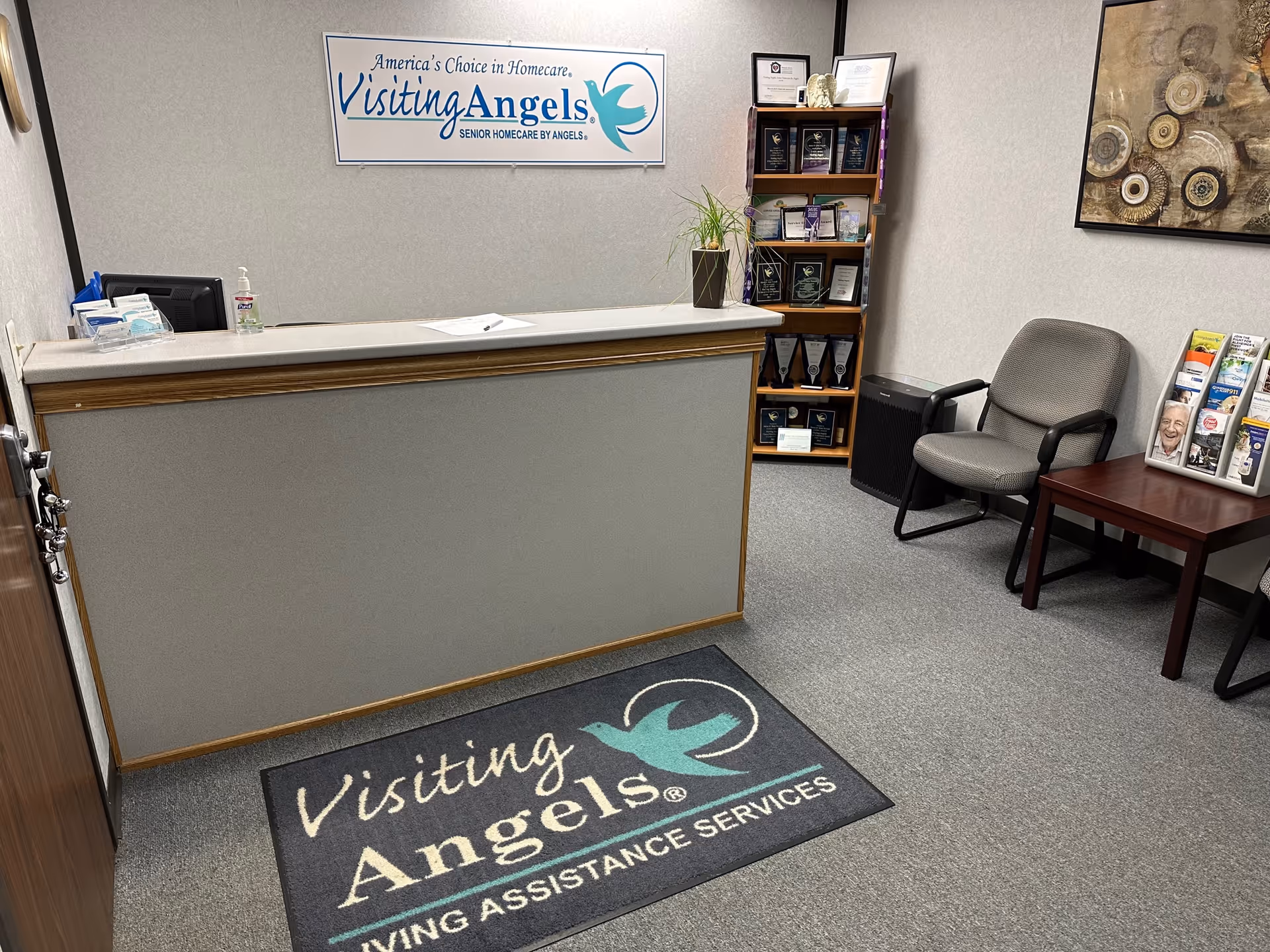 Reception area of Visiting Angels Senior Home Care with desk, chairs, and awards display.