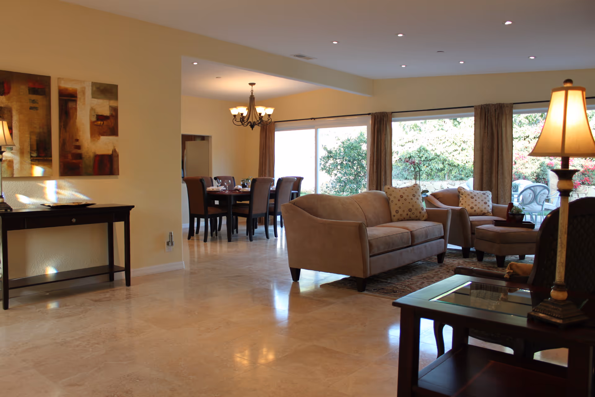 Spacious senior living lounge with beige sofas, chairs, coffee tables, and large windows.