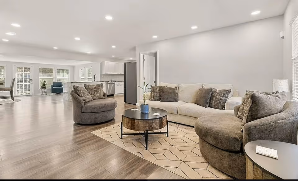 Bright open living room in a senior facility with neutral furniture and a visible kitchen.