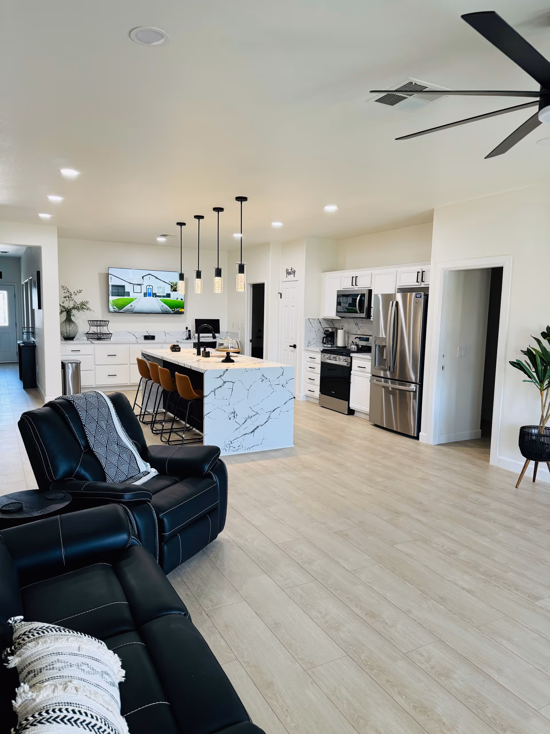 Open-concept living area with marble island, white cabinets, stainless appliances, and black seating.