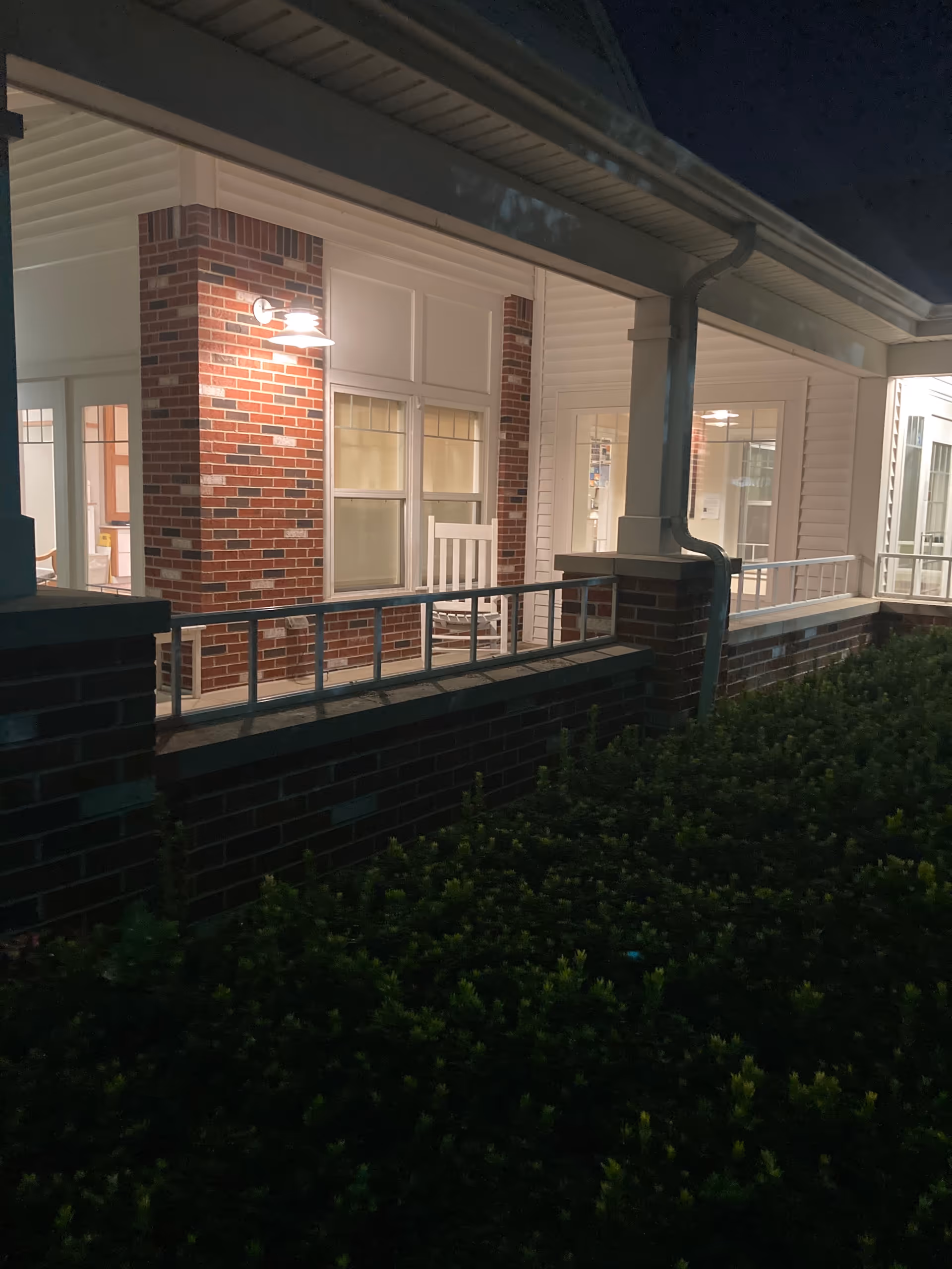 Nighttime exterior of Medilodge of Monroe with brick walls, a porch, and railing.