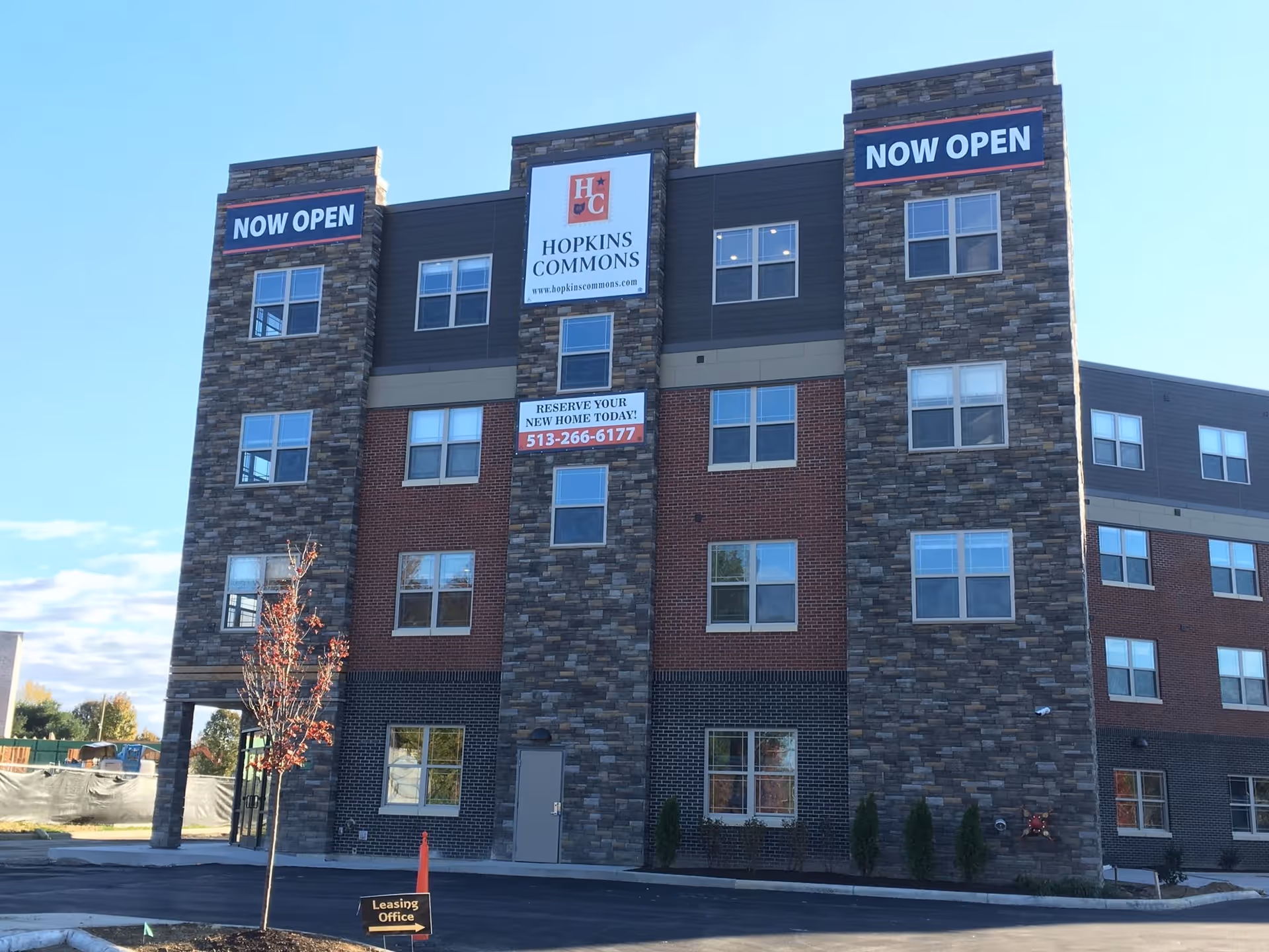 Four-story Hopkins Commons residential building with a stone-and-brick facade and 'NOW OPEN' signs.