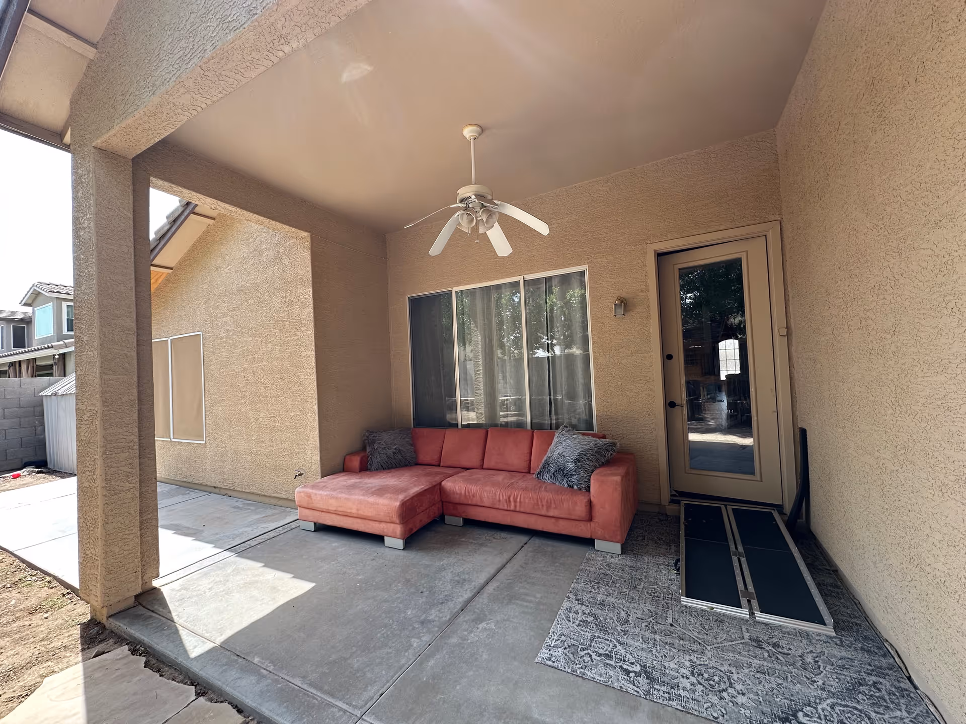 Covered patio outside with coral sectional sofa, ceiling fan, glass door, and entry steps.
