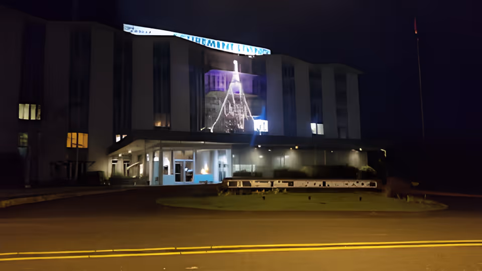 Front exterior of a multi-story senior residence building at night with an illuminated entrance and light projection on the façade.