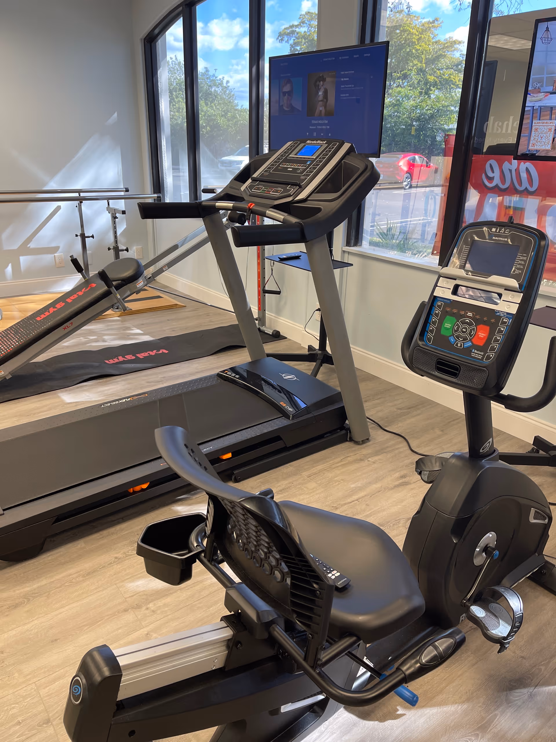 Indoor fitness room with treadmill, stationary bike, and large windows.