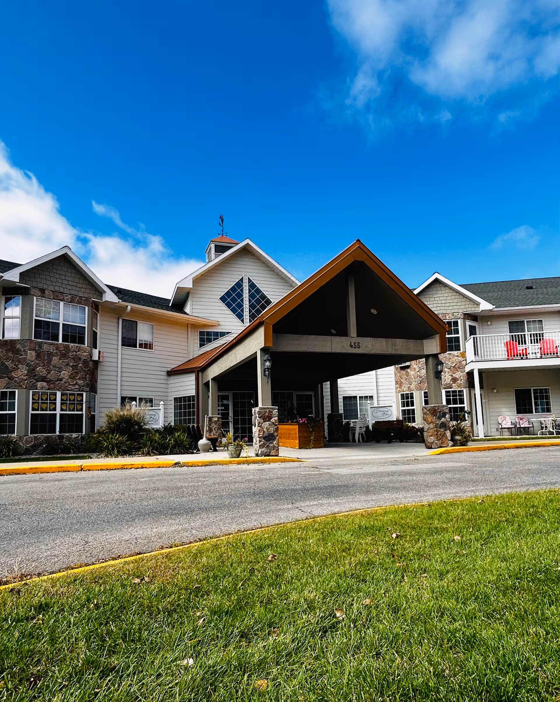 Front view of Harmony Place senior living facility entrance with porte-cochere and landscaping.