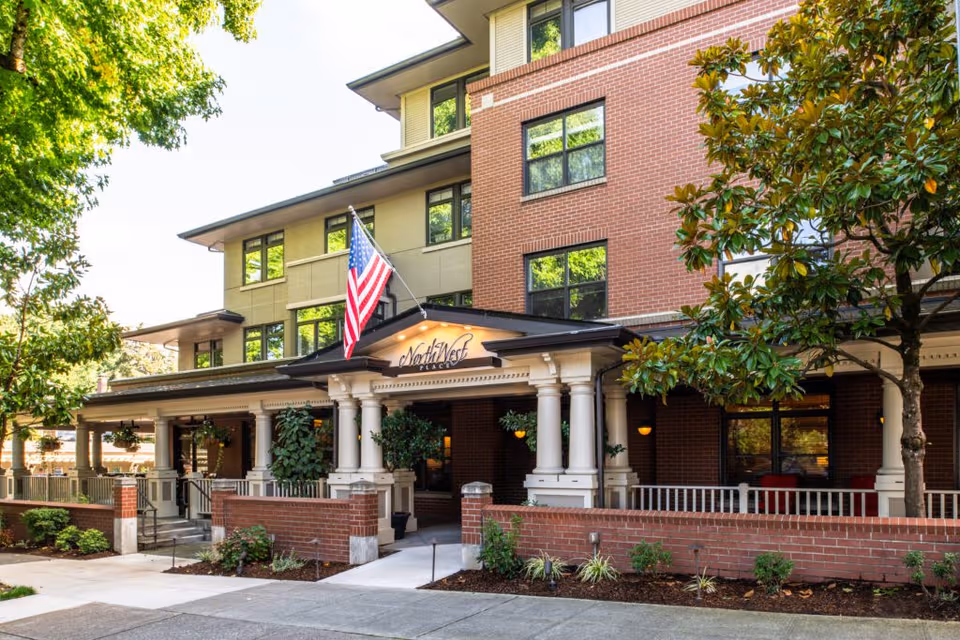 Exterior view of NorthWest Place senior living entrance with brick facade, columns, and flag.