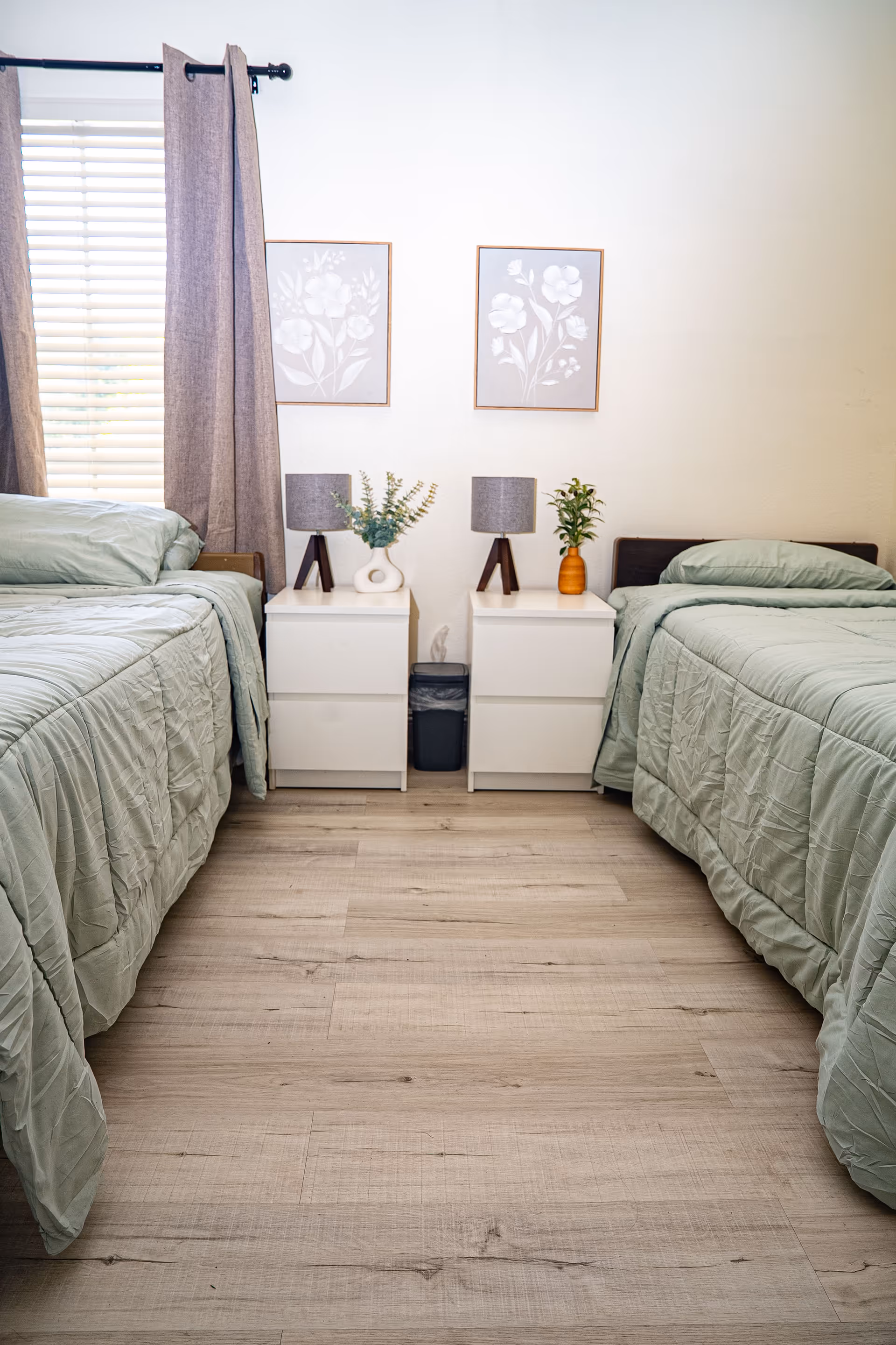 Two twin beds with nightstands, lamps, and soft green bedding in a tidy bedroom.