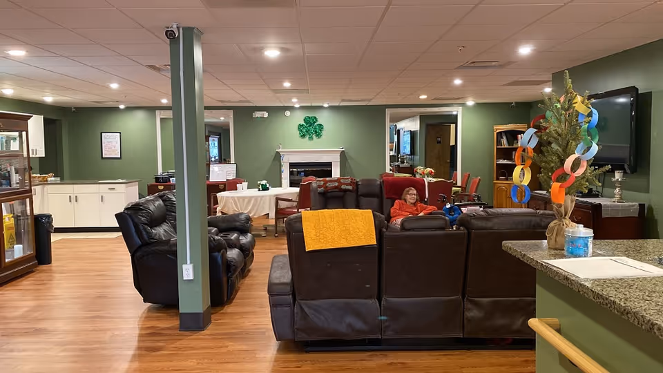 Lounge area with green walls, brown leather couches, residents relaxing near a fireplace.
