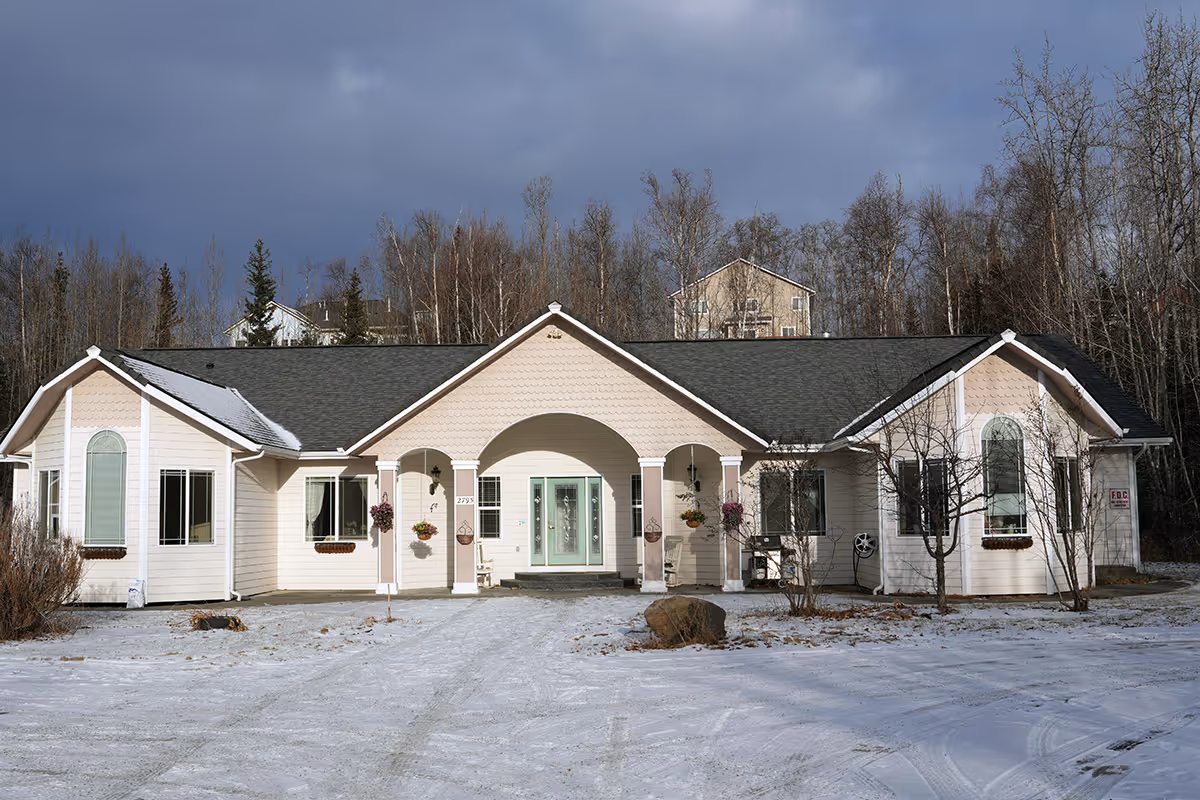 Light-colored, single-story building with arched entryway and snow on the ground.