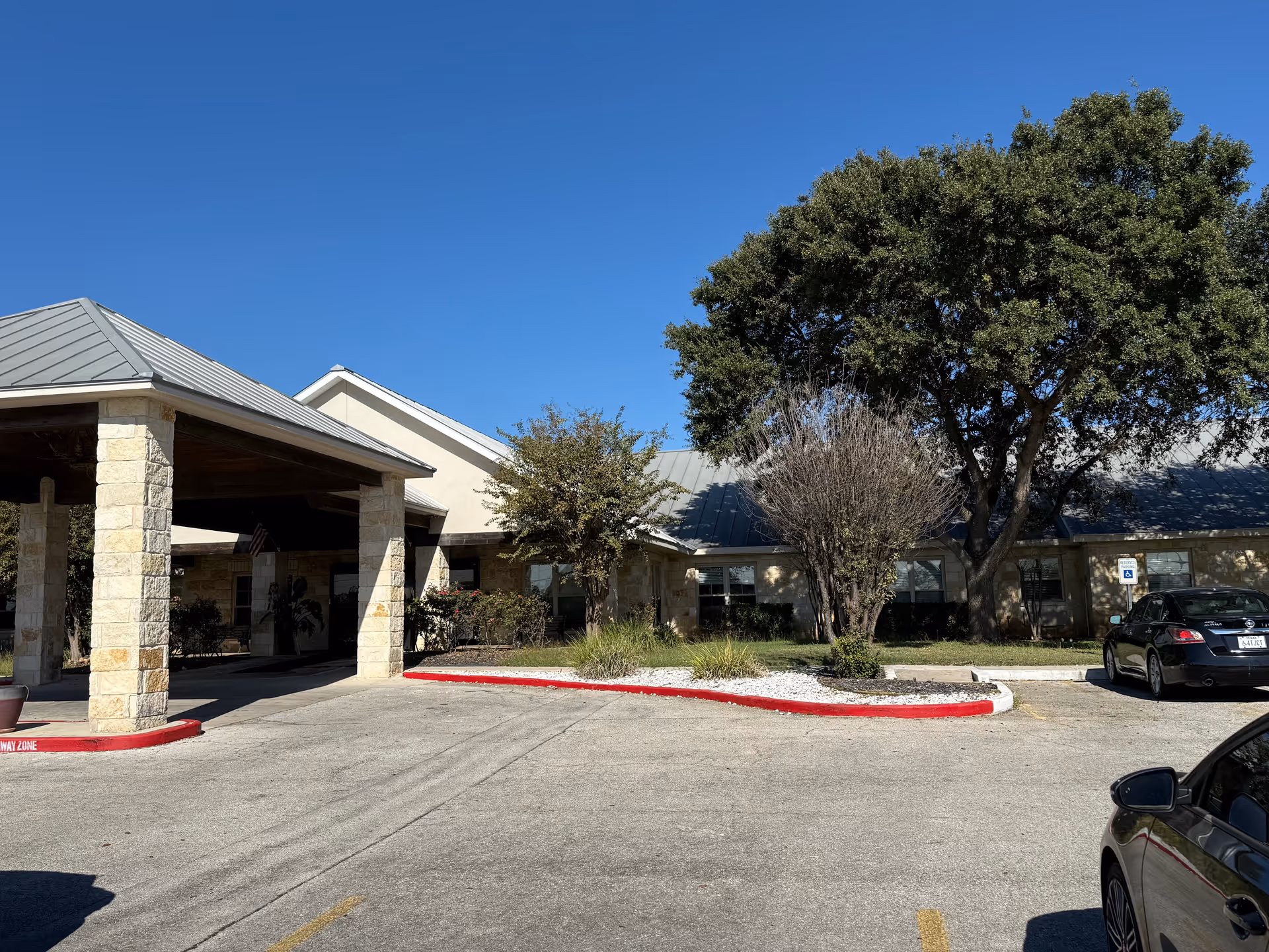 Meridian Care facility entrance with stone pillars, trees, and parked cars.