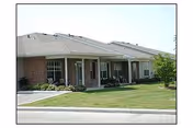 Front exterior of a single-story brick senior living building with a covered entrance and lawn.