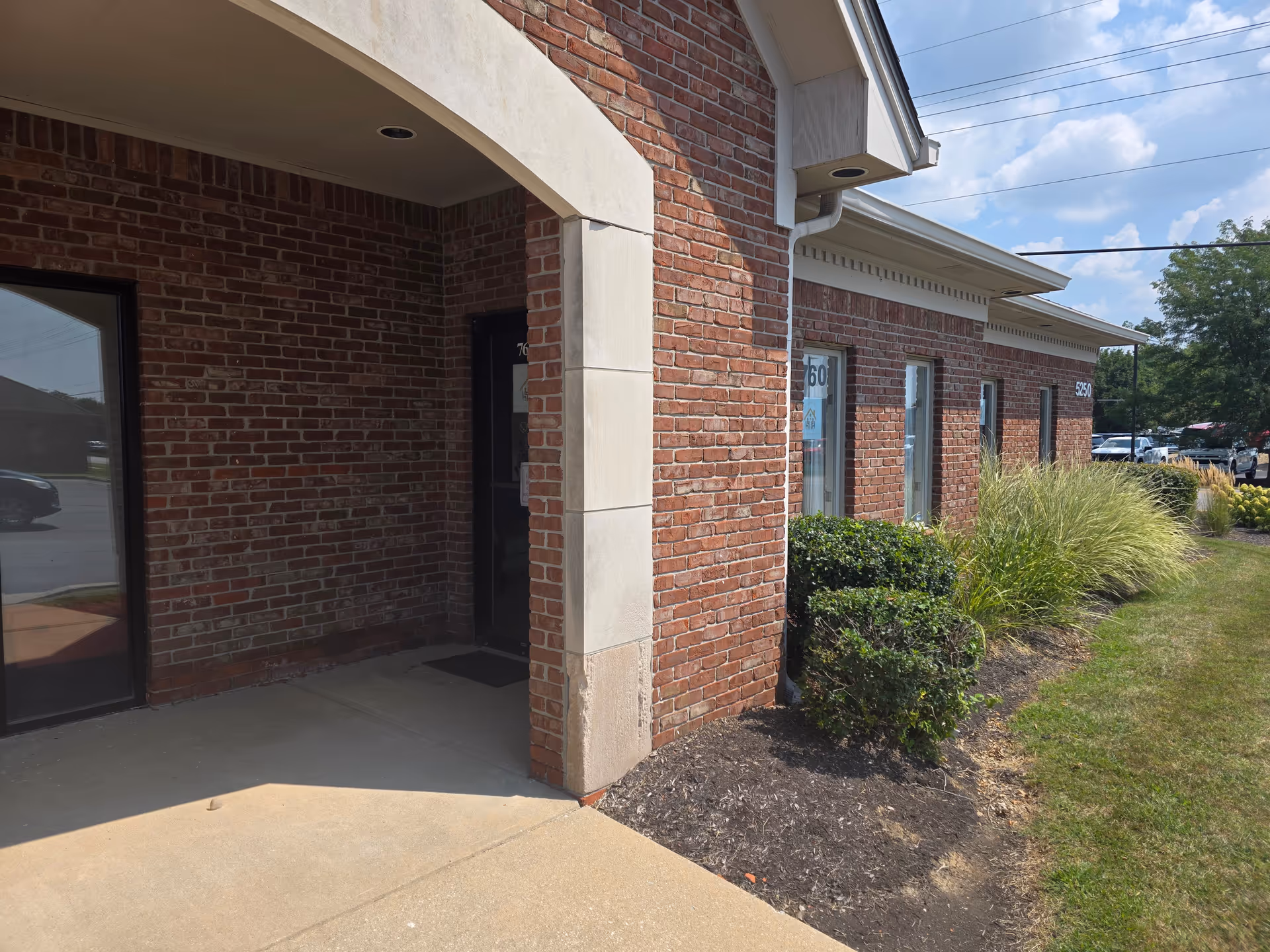 Brick exterior of a facility entrance with shrubs and landscaping along the walkway.