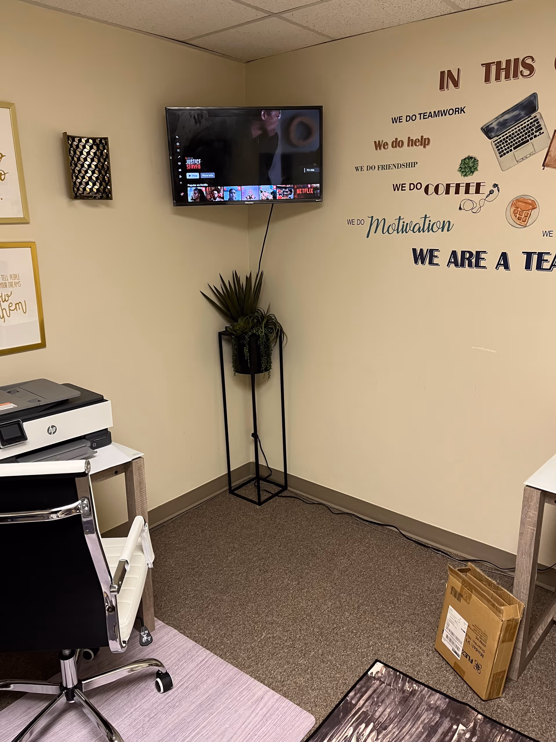 Office corner in a senior living facility with desk, printer, mounted TV, and plant.