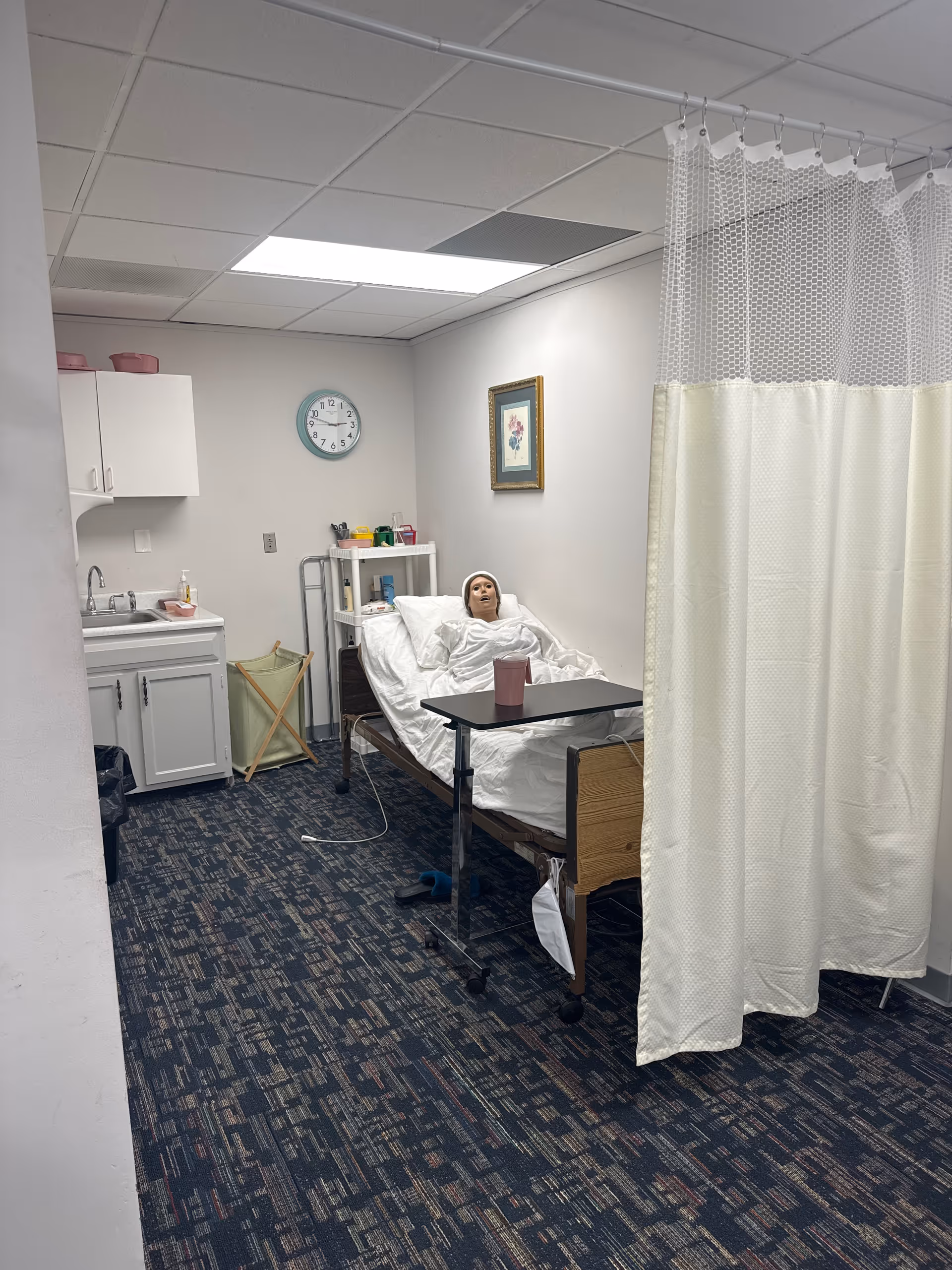 A patient lies in a hospital bed beside a white privacy curtain in a clinical room.