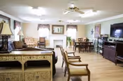 A spacious senior living room with sofa, chairs, fireplace, lamps, and a dining area in back.