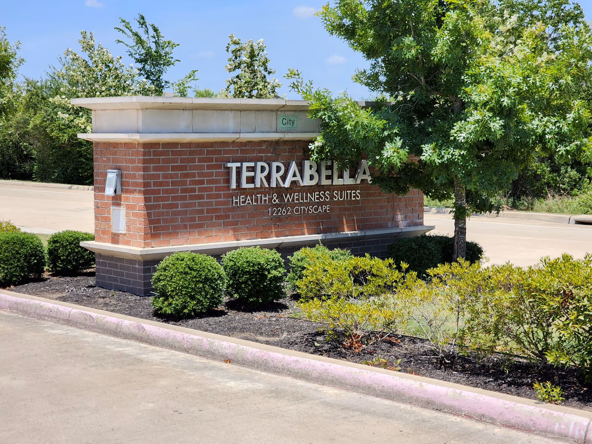 Brick sign for TerraBella Health & Wellness Suites with greenery along the front.