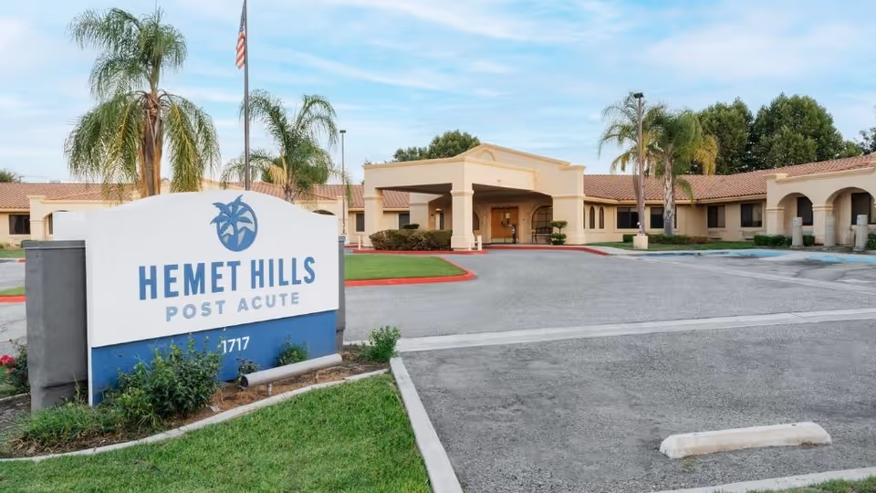 Exterior view of ManorCare Hemet Hills Post Acute facility with entrance sign and palm trees.