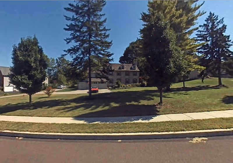 Exterior view of a multi-story building with trees, lawn, and a sidewalk.