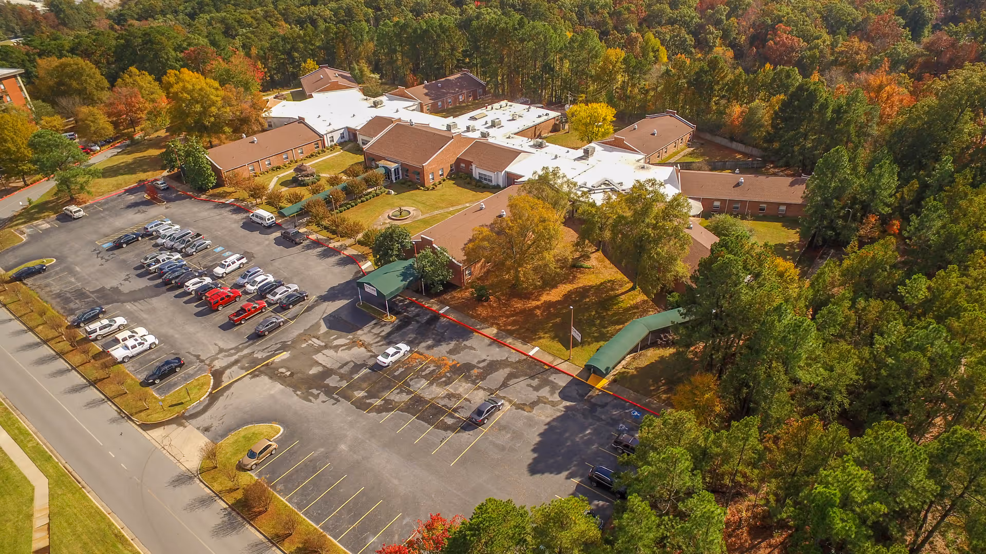 Aerial view of a nursing facility and its parking lot surrounded by trees with autumn foliage.