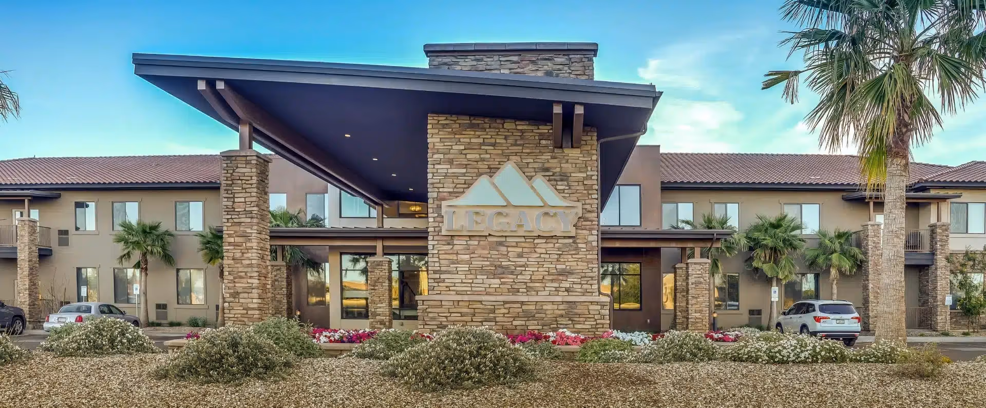 Front exterior of Legacy House of Avondale showing the stone entrance with a 'LEGACY' sign, palm trees, and parked cars.
