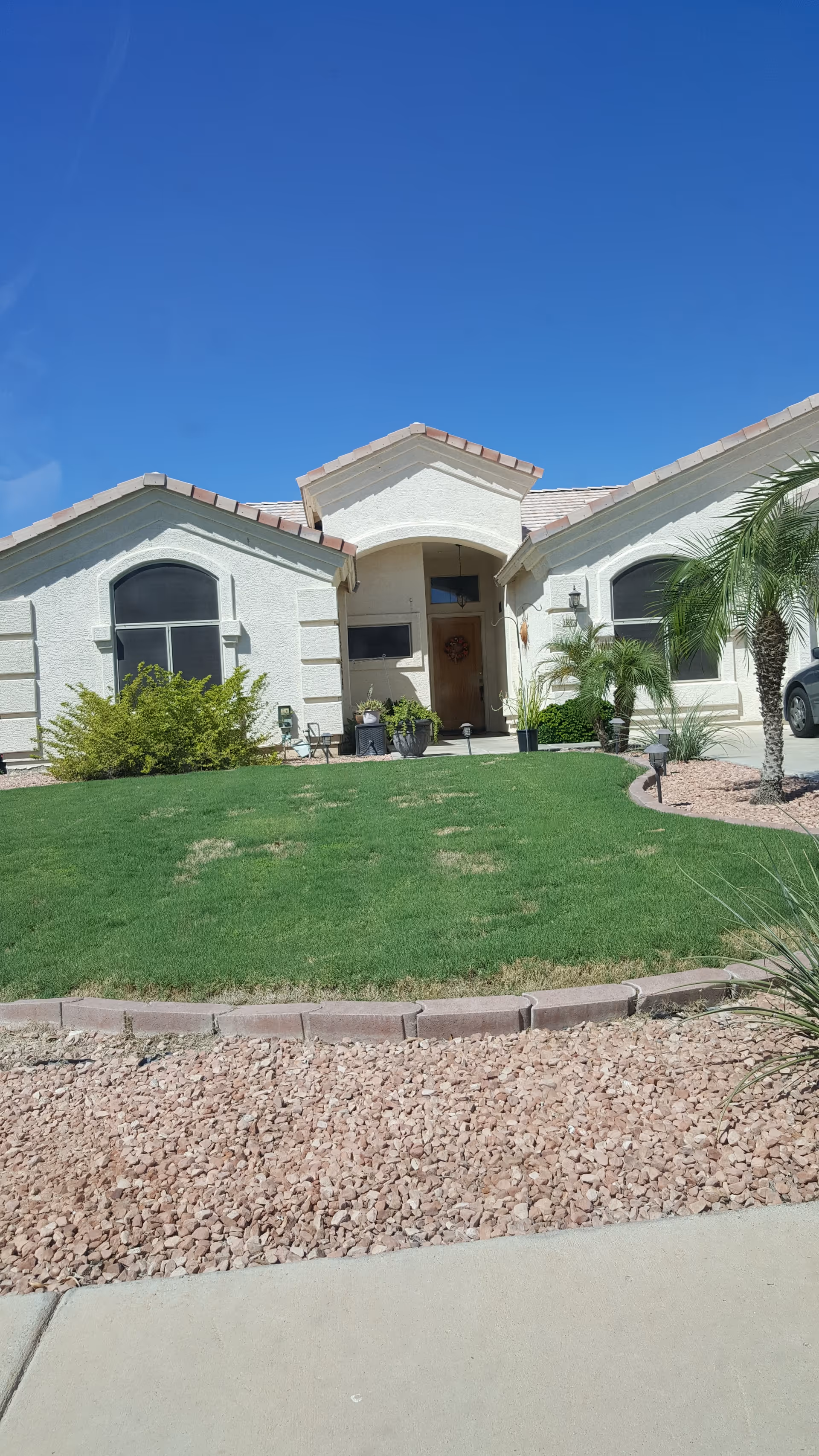 Front view of a single-story senior living facility with a green lawn and palm trees.