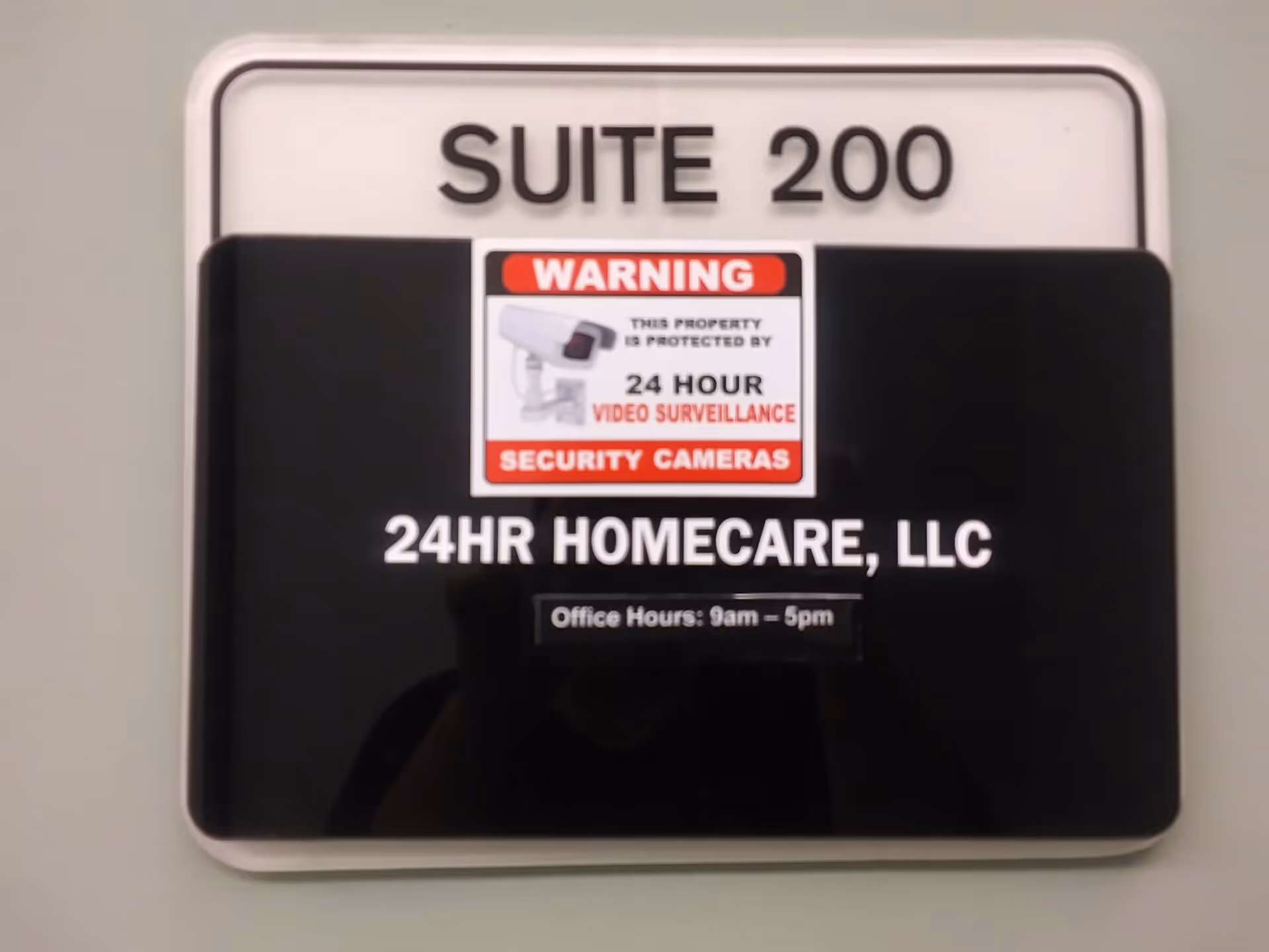 Interior wall sign reading Suite 200 for 24HR Homecare, with a security camera sticker