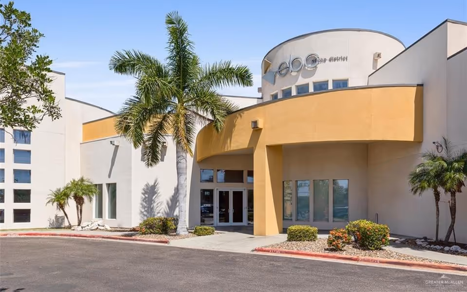 Exterior view of a modern senior living facility entrance with palm trees and glass doors.