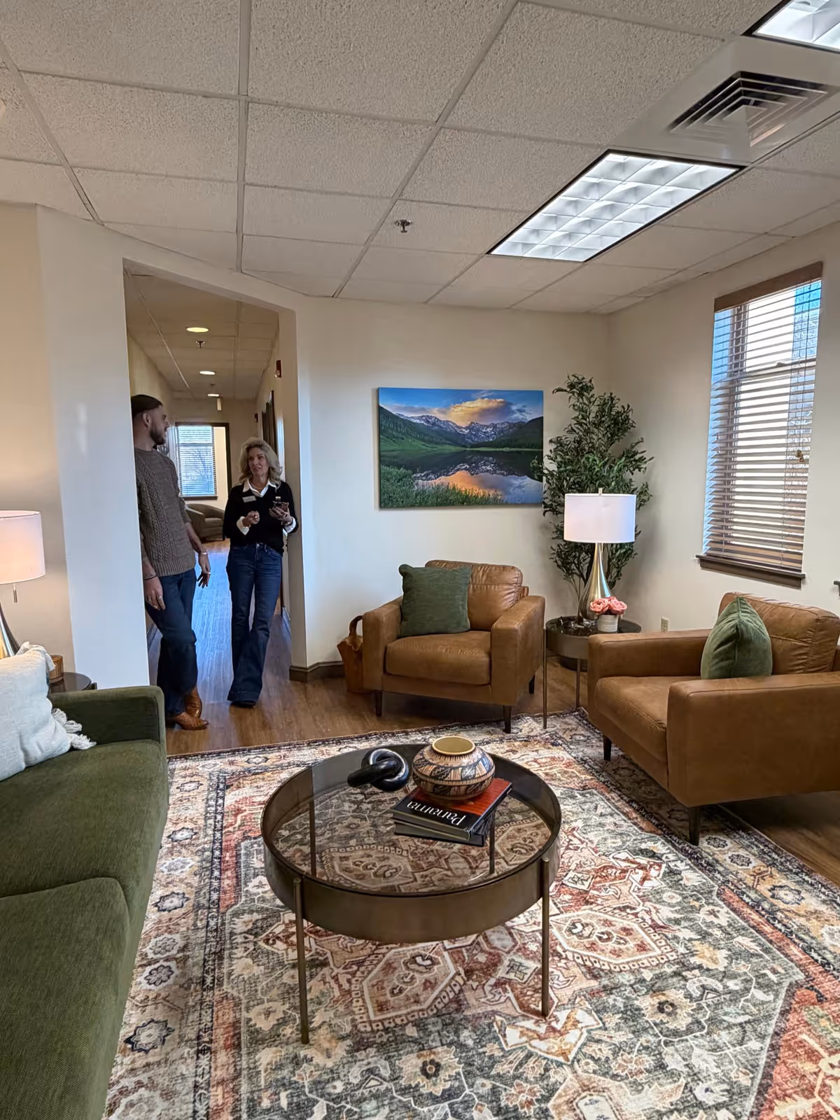 Two people stand near a doorway in a warm living room lounge with seating.