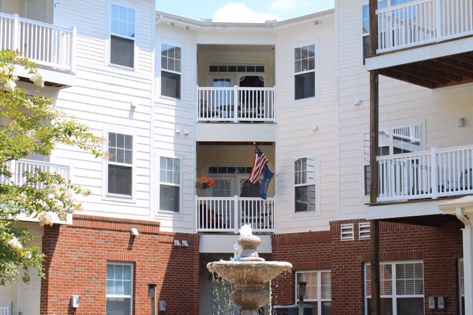 Three-story brick-and-siding senior living building with white balconies overlooking a central courtyard fountain.