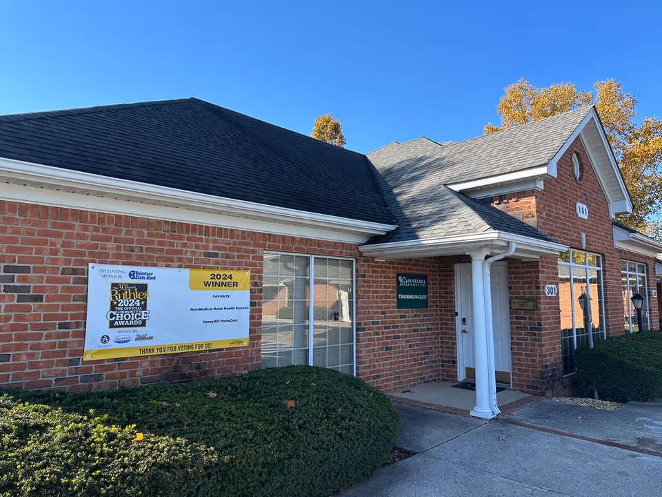 Brick HoneyHill HomeCare facility exterior with banner, entrance, and manicured shrubs under blue sky.