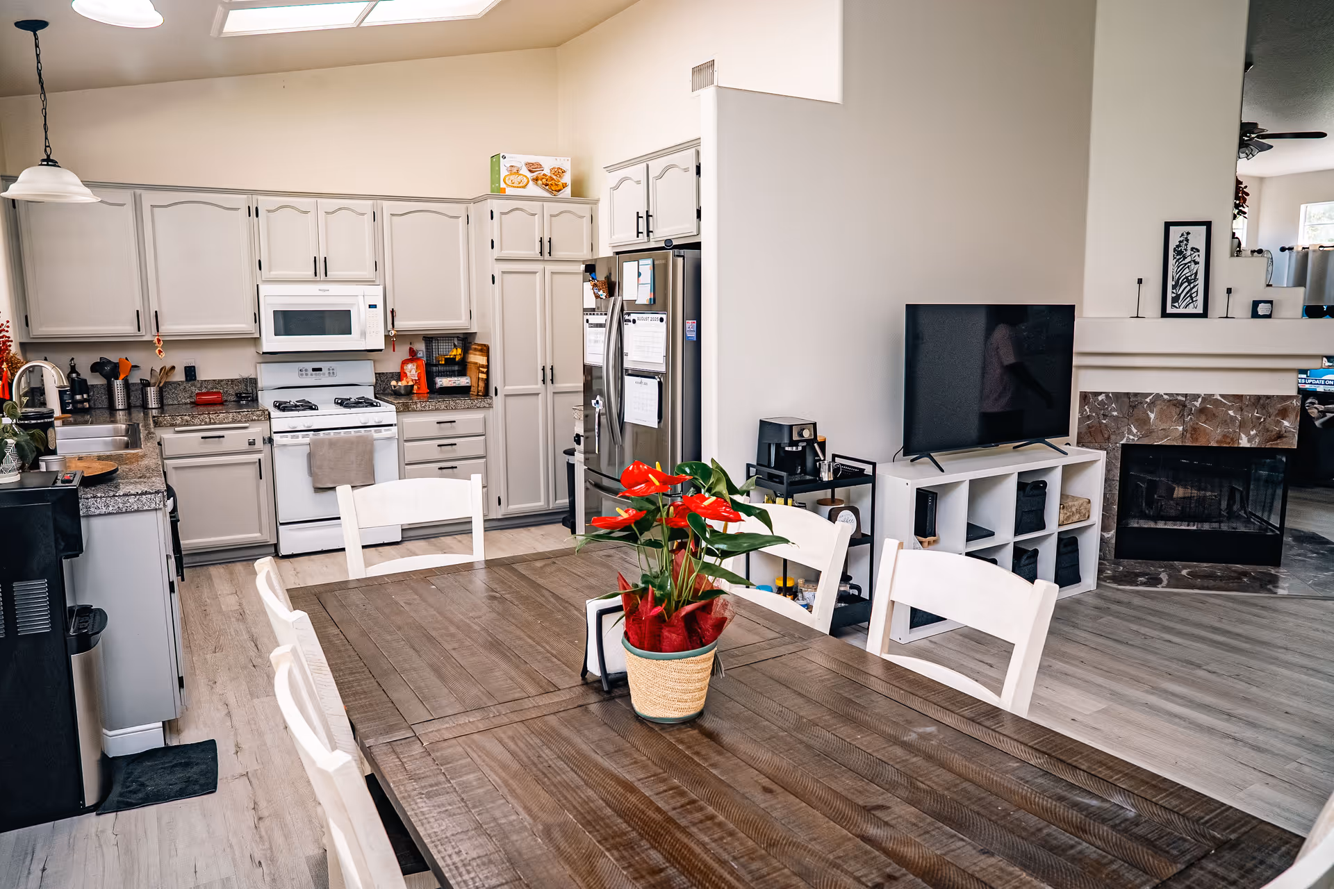 Open-concept kitchen and dining space with wooden table, white chairs, and a TV.