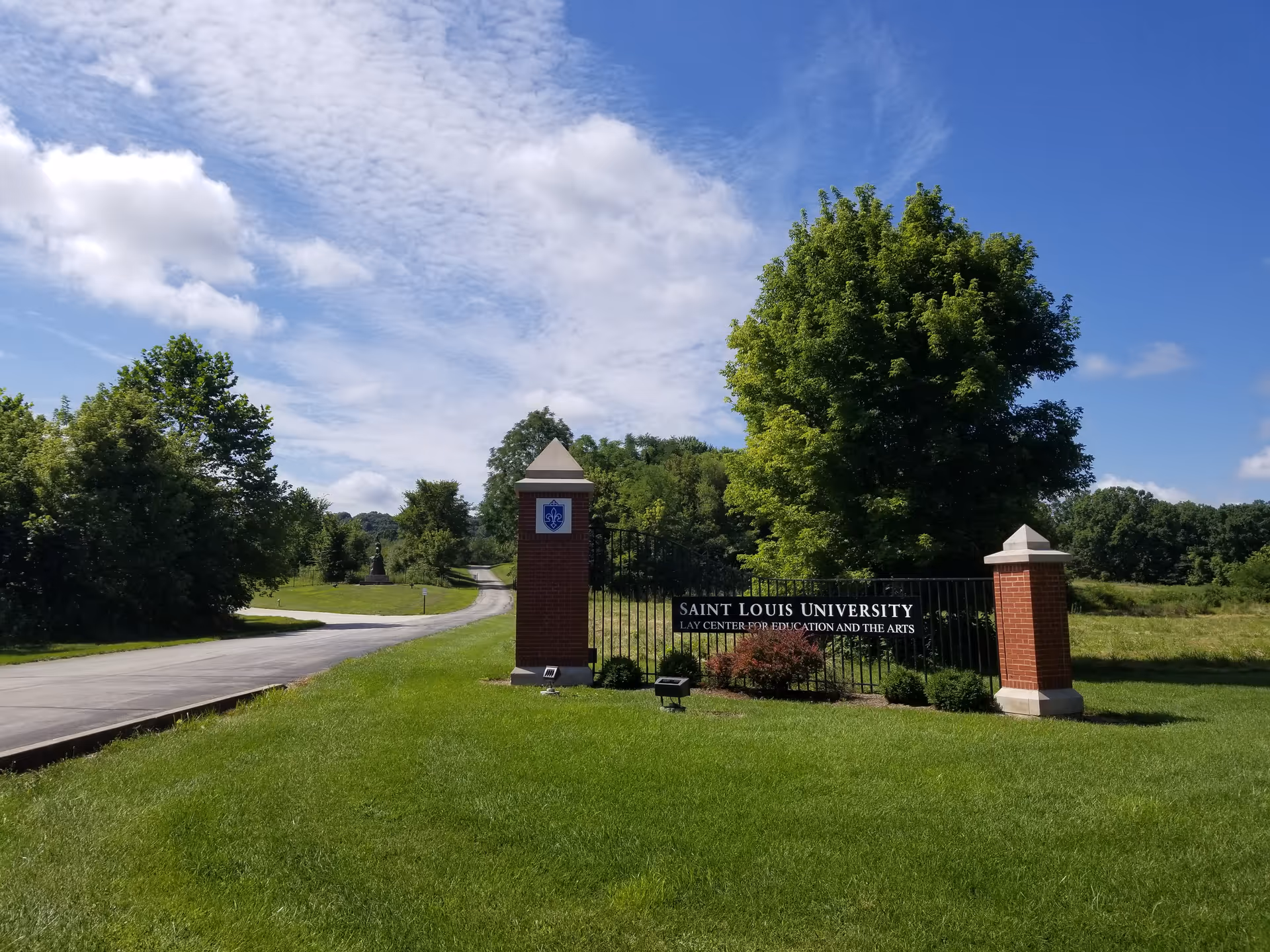 Outdoor campus entrance with brick pillars and sign for Saint Louis University Lay Center amid greenery.