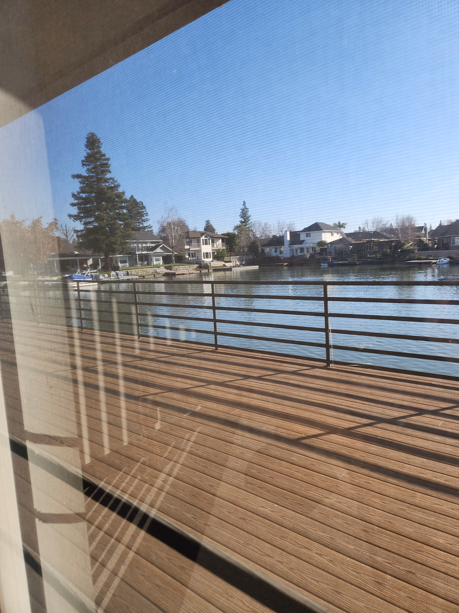 Wood deck with metal railing overlooks a lake and houses on the opposite shore.
