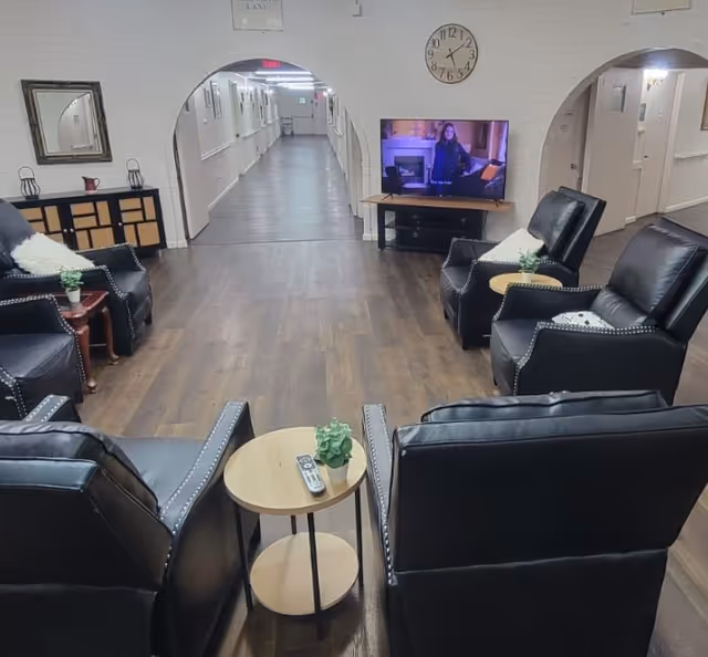 A spacious senior living lounge with black leather chairs, small tables, and a TV.