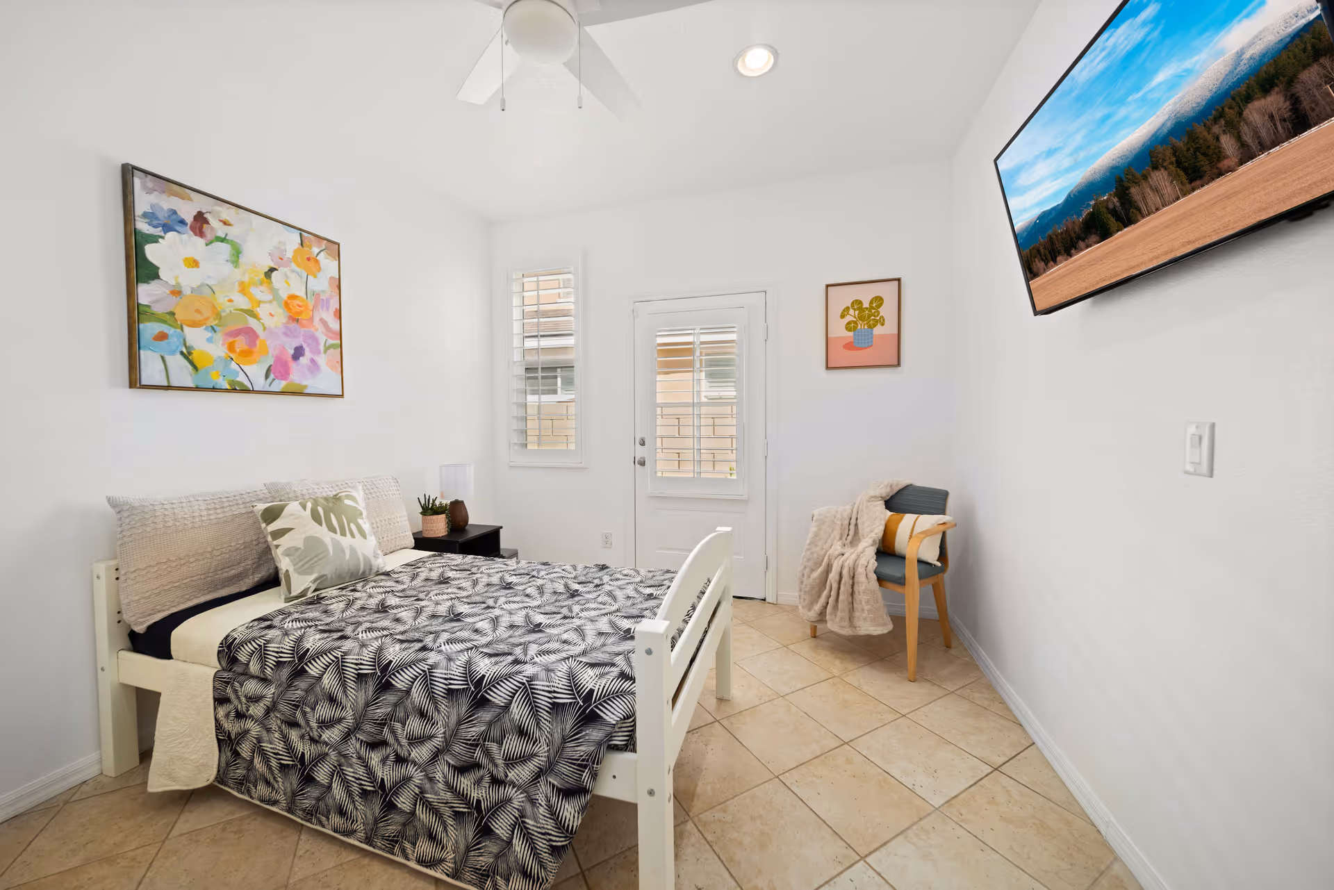 Bright compact bedroom in a senior living facility with bed, chair, TV, and art.