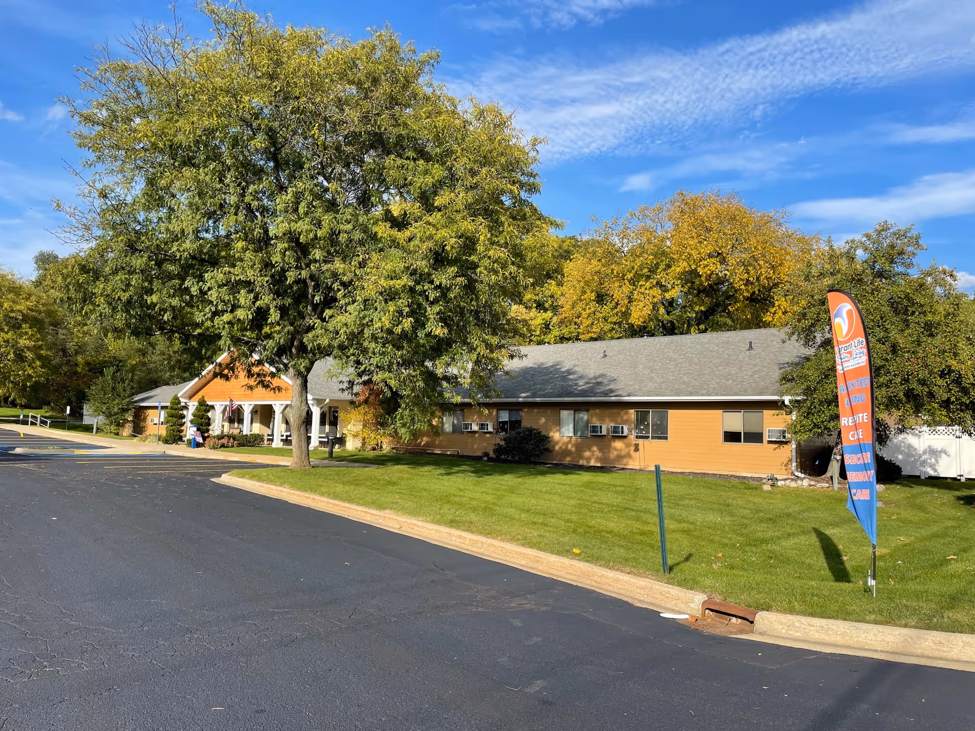 Exterior view of a single-story tan senior care facility with a lawn and trees.