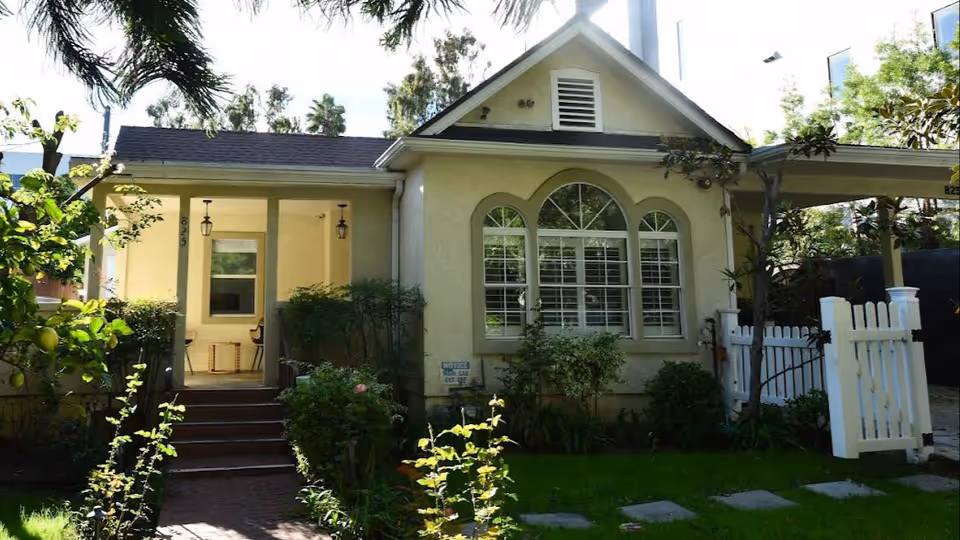 Single-story light-colored senior facility with arched windows, front porch, gate, and garden.