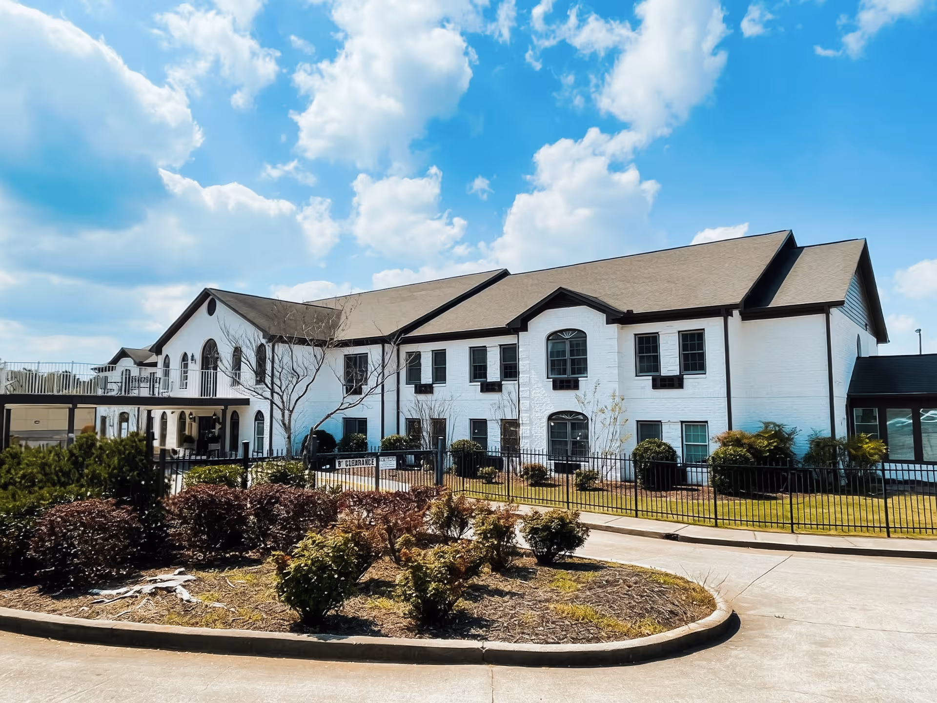 White brick senior living building with black trim, landscaped front, under blue sky.