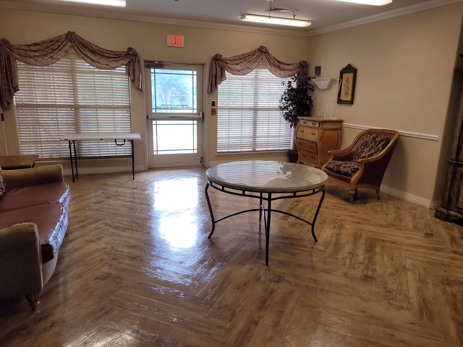 Interior lounge in a senior living facility with sofa, armchair, and glass coffee table.