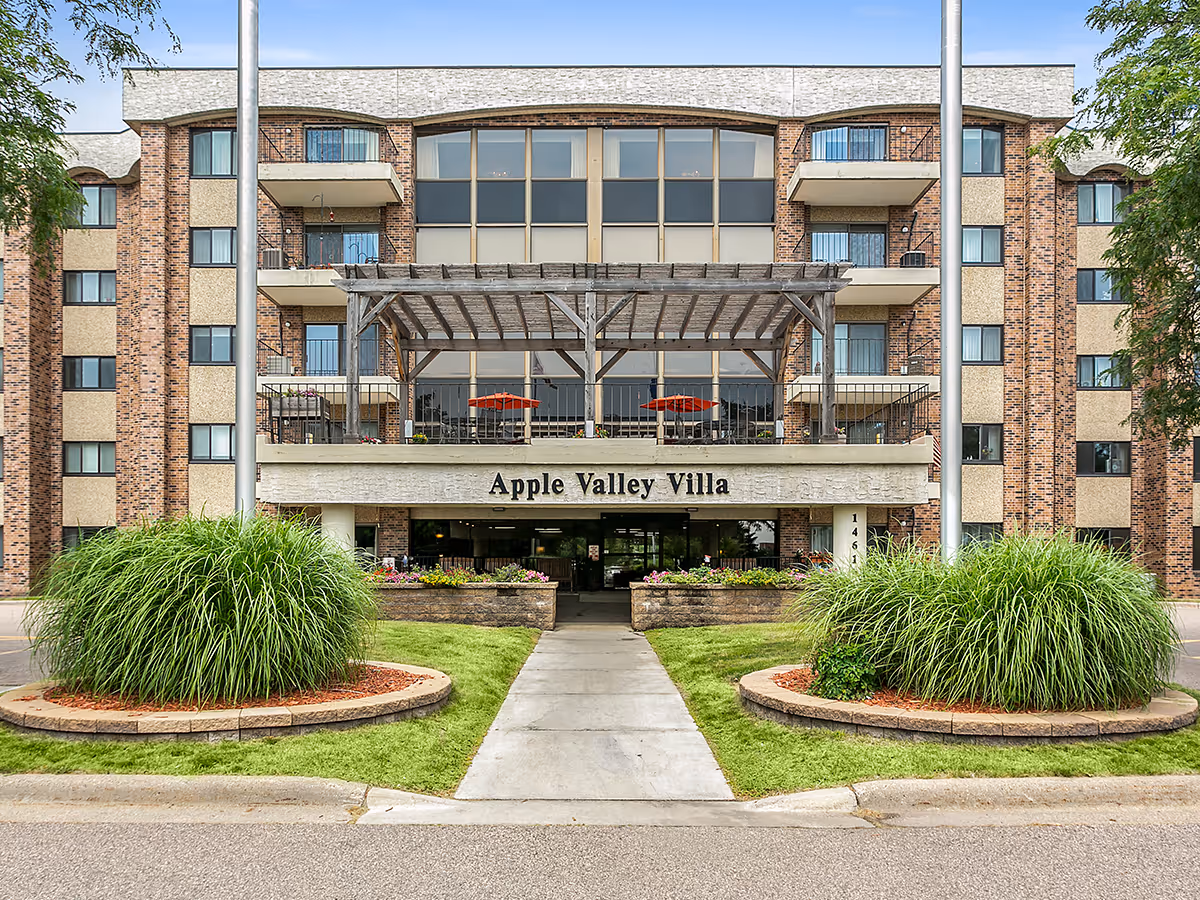 Front view of Apple Valley Villa building with entrance walkway and landscaped circular plant beds.