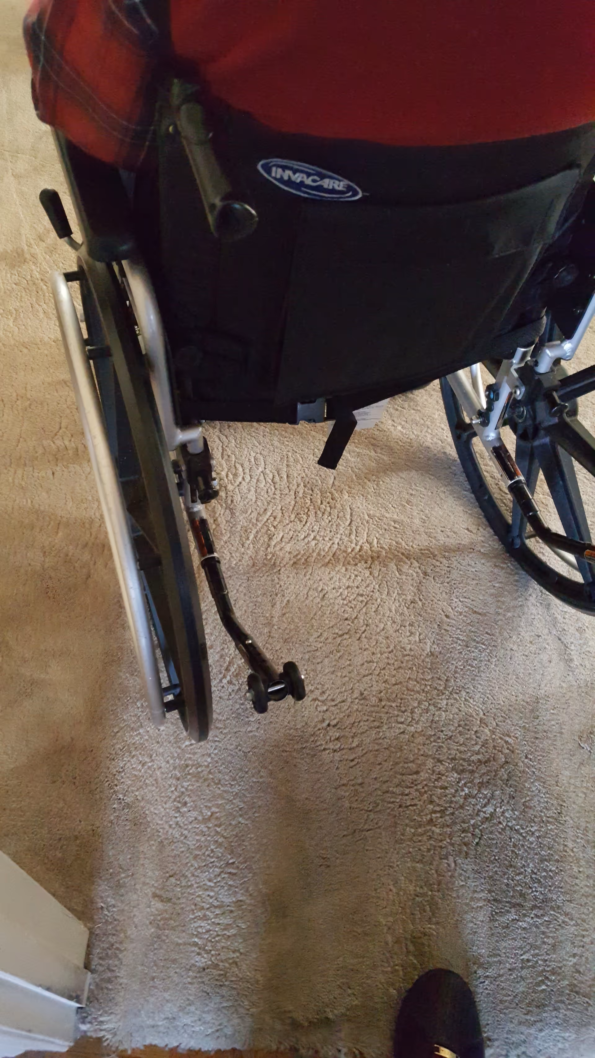 Wheelchair on tan carpet inside a facility hallway, with a shoe visible.