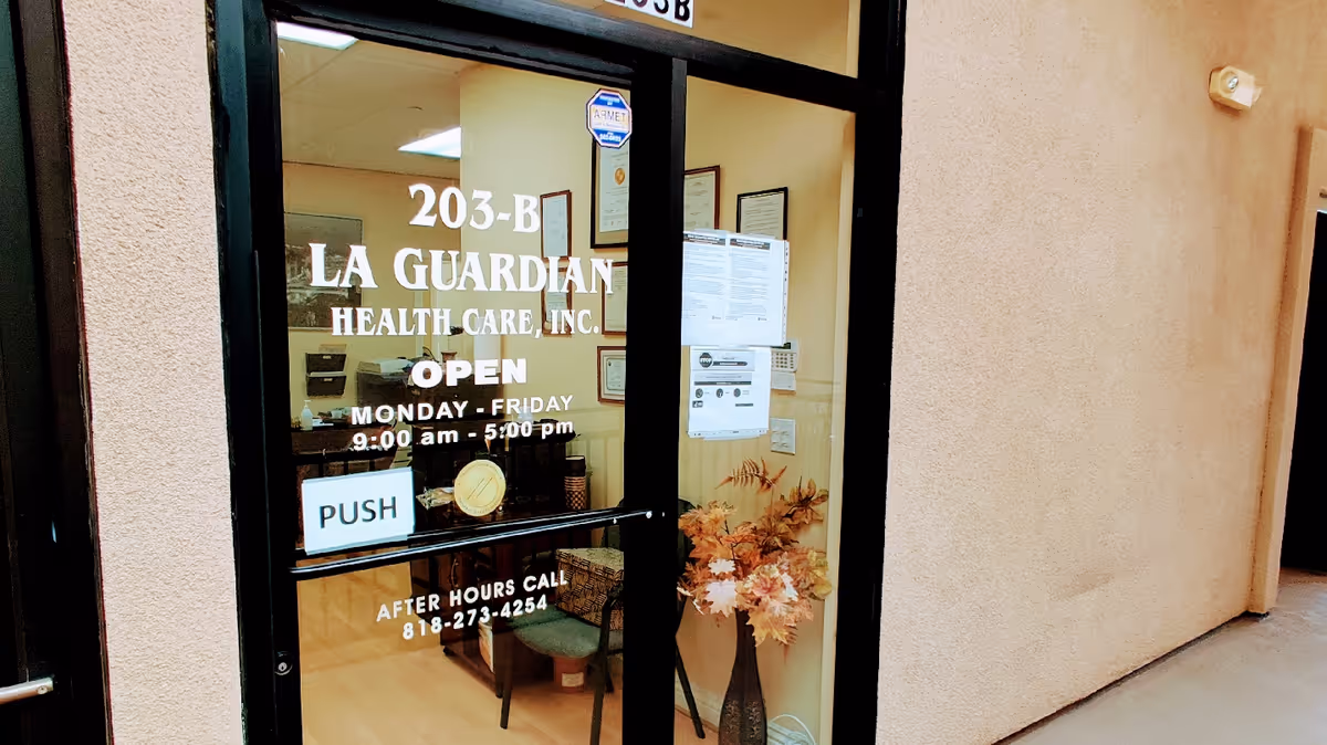 Glass entrance door for La Guardian Health Care with hours and plants visible.