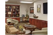 A cozy senior living lounge with couches, coffee tables, shelves, and wall art.