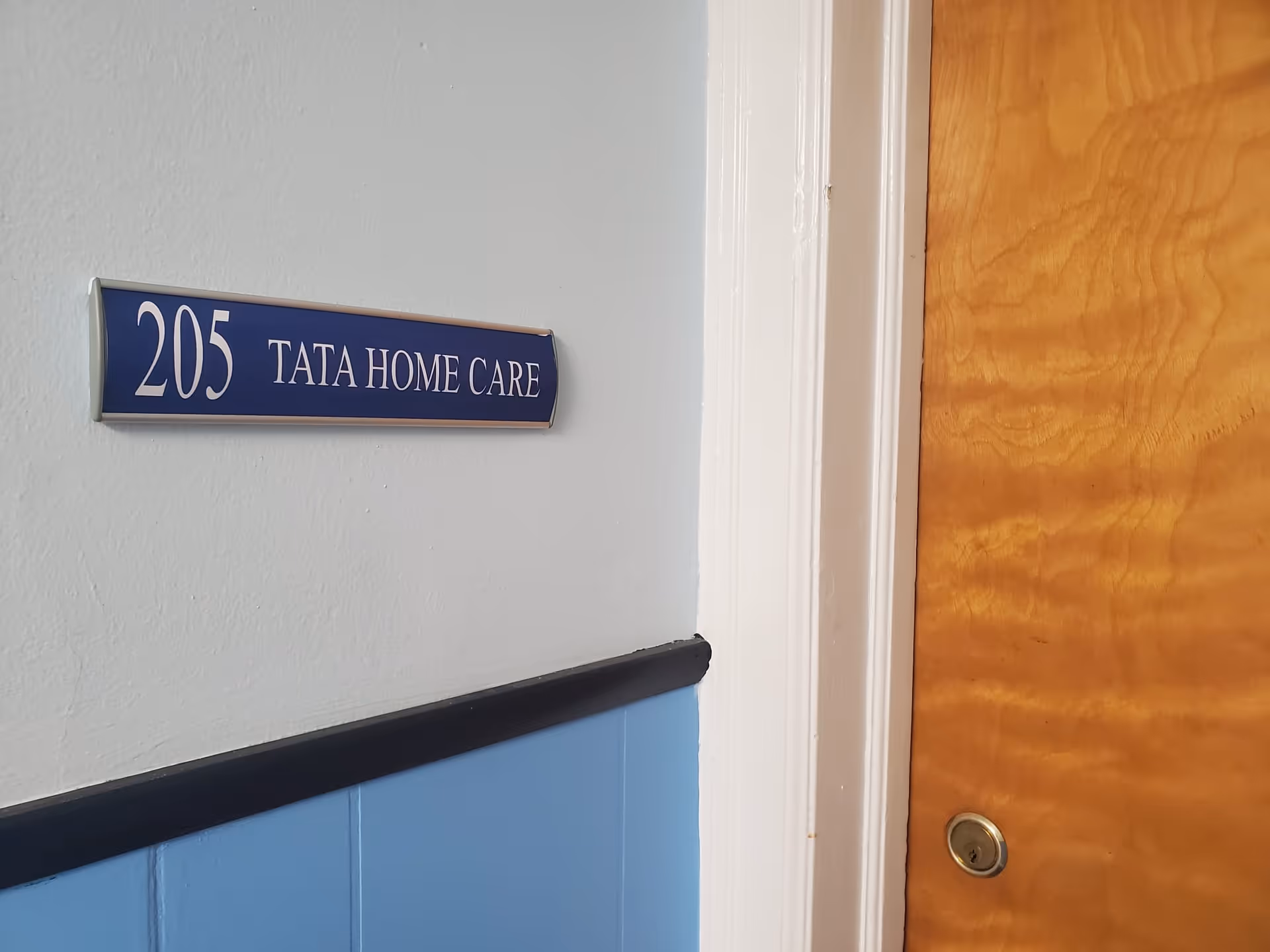 Interior wall with blue wainscoting and a hallway door labeled 205 TATA HOME CARE