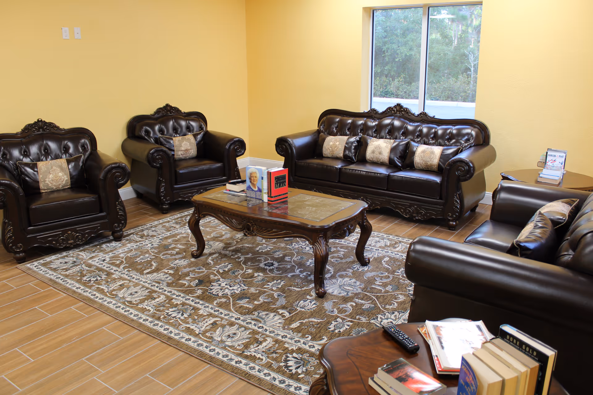 Brown leather seating surrounds a central wooden coffee table in a senior living lounge.