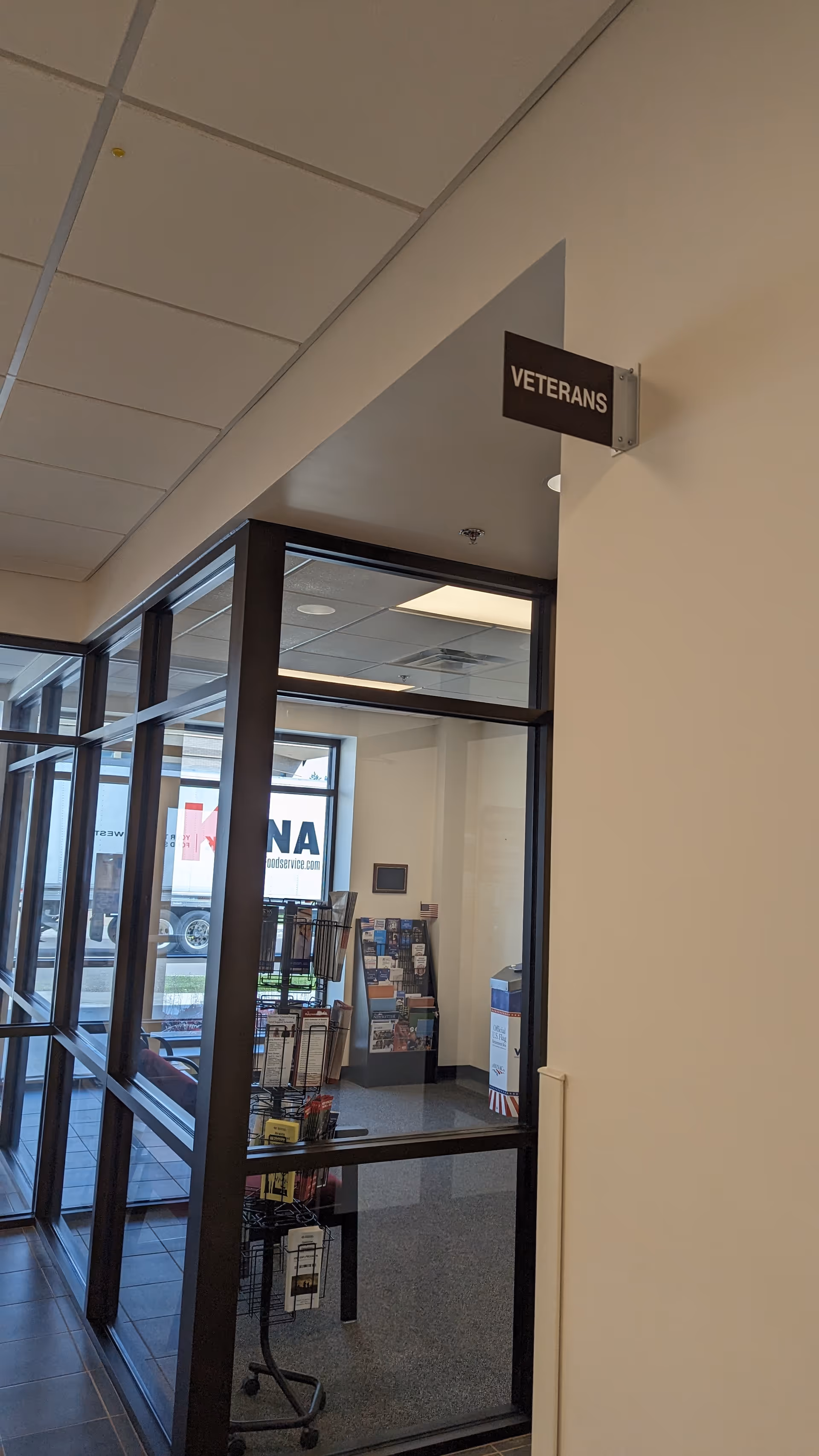Hallway with glass storefronts, a sign reading Veterans, and a magazine rack inside.