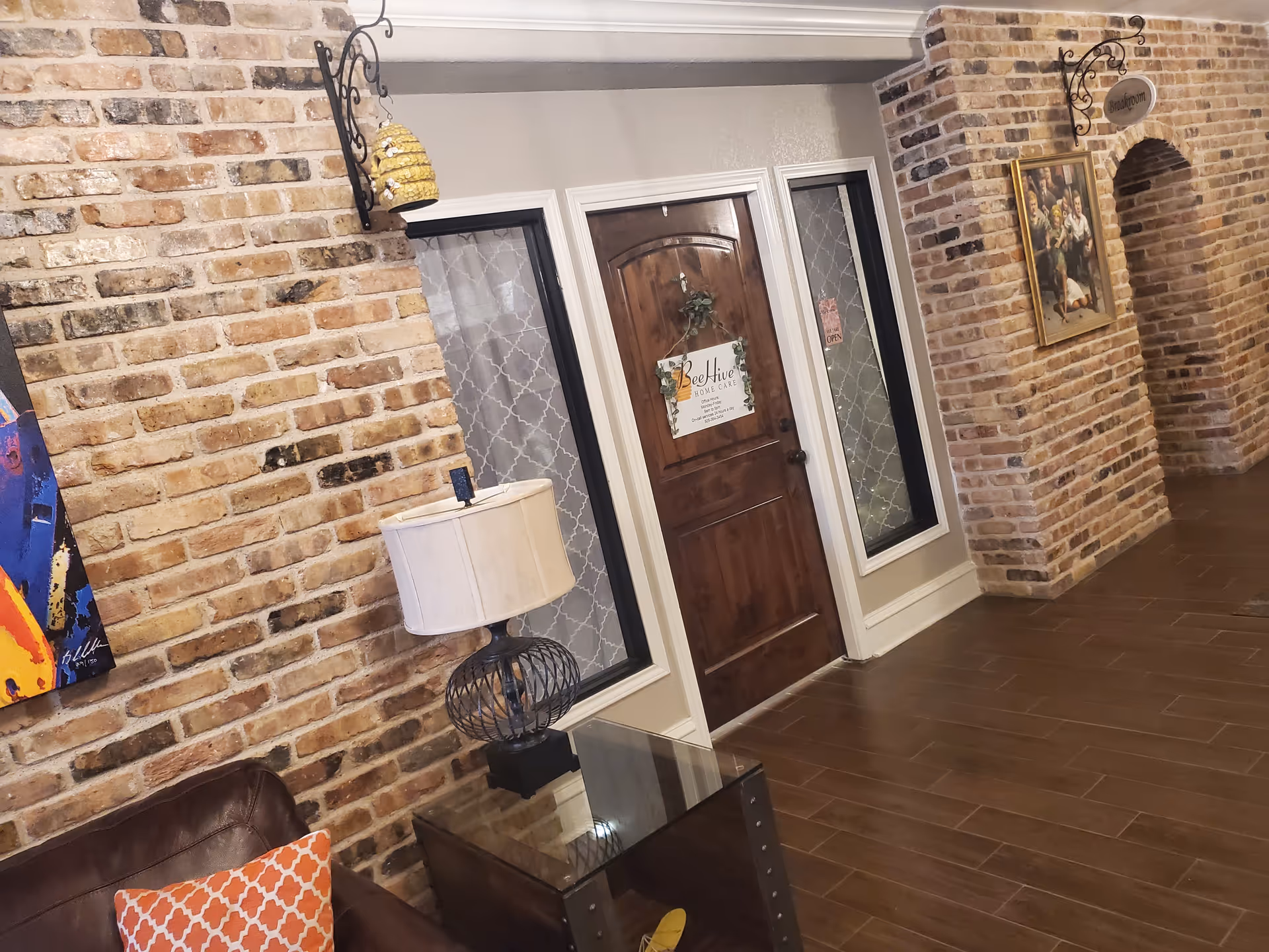 Indoor brick hallway with a Beehive Home Care door, lamp, sofa, and artwork.