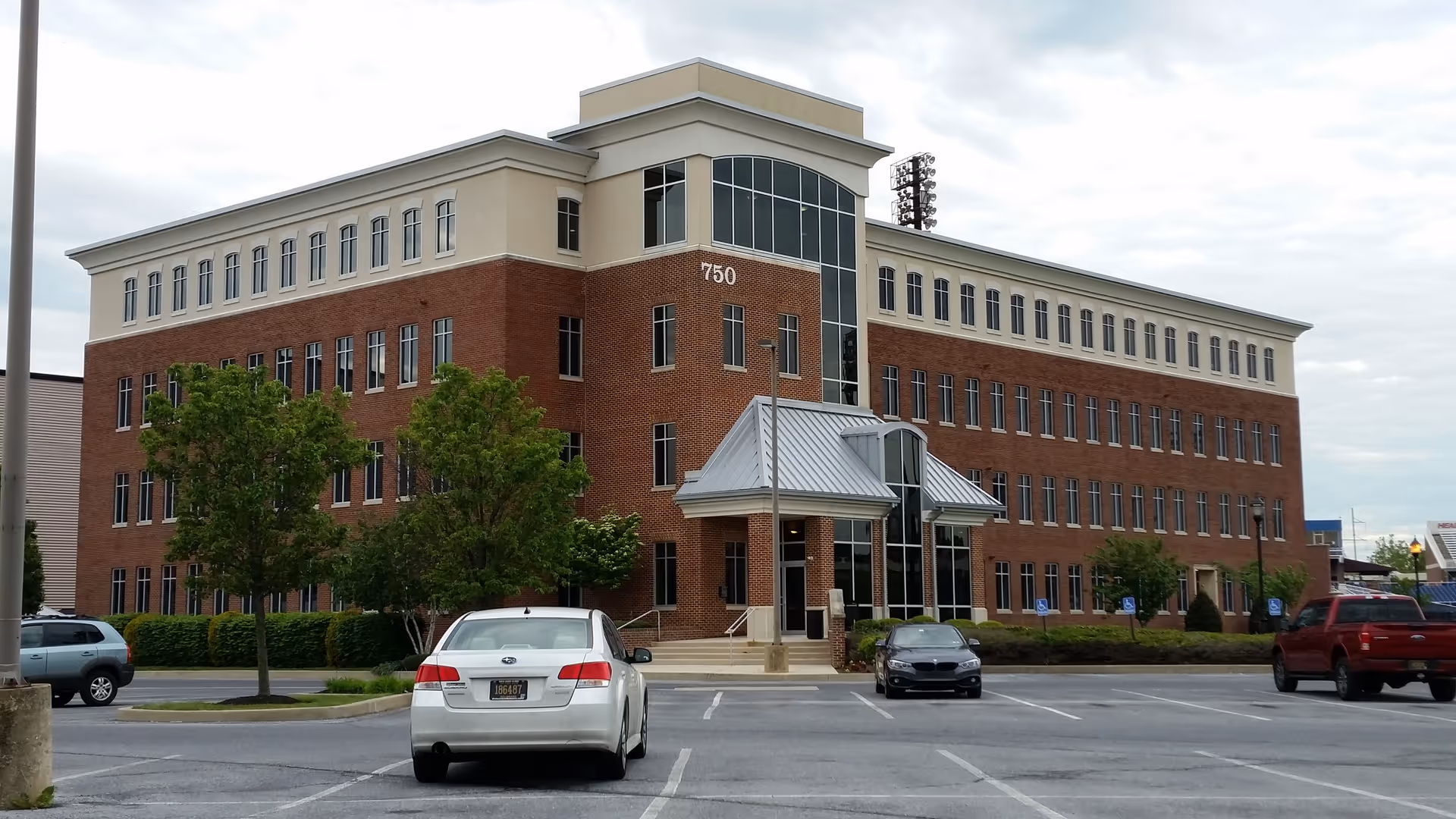 Front view of a brick building with a glass entry and parked cars.
